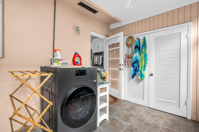 clothes washing area with tile patterned floors, washer / clothes dryer, and wood walls