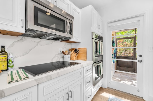 kitchen with white cabinets, appliances with stainless steel finishes, light hardwood / wood-style flooring, and light stone countertops