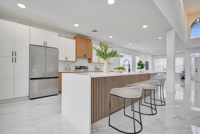 kitchen featuring a center island with sink, a kitchen bar, white cabinetry, and appliances with stainless steel finishes