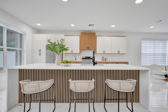 kitchen featuring sink, white cabinetry, range with electric stovetop, a breakfast bar area, and an island with sink