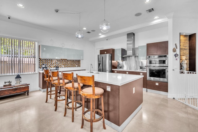 kitchen featuring decorative backsplash, appliances with stainless steel finishes, dark brown cabinetry, wall chimney range hood, and a center island with sink