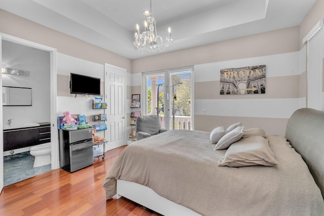 bedroom featuring a chandelier, wood-type flooring, ensuite bathroom, and a raised ceiling