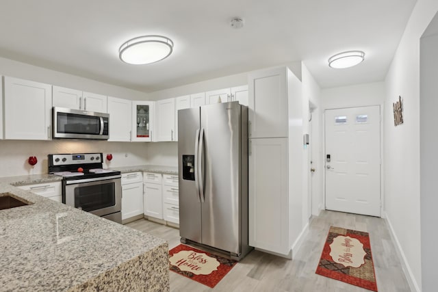 kitchen with light stone countertops, appliances with stainless steel finishes, sink, light hardwood / wood-style flooring, and white cabinetry