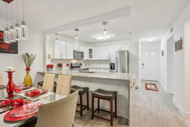 kitchen featuring kitchen peninsula, light wood-type flooring, stainless steel appliances, decorative light fixtures, and white cabinets