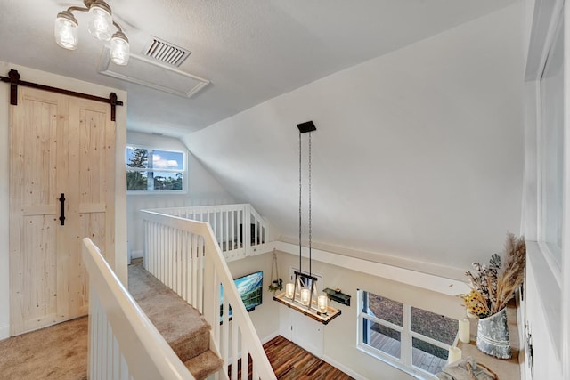 bedroom featuring a textured ceiling, wood-type flooring, a barn door, a nursery area, and lofted ceiling