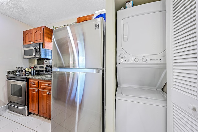 kitchen featuring dark stone counters, a textured ceiling, light tile patterned flooring, stacked washer and clothes dryer, and appliances with stainless steel finishes