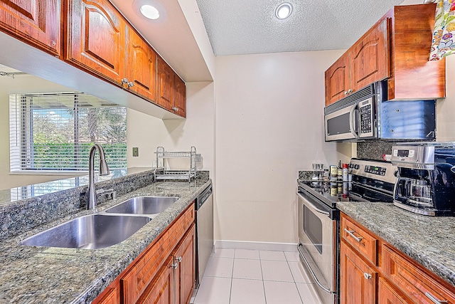 kitchen with dark stone counters, a textured ceiling, stainless steel appliances, sink, and light tile patterned flooring