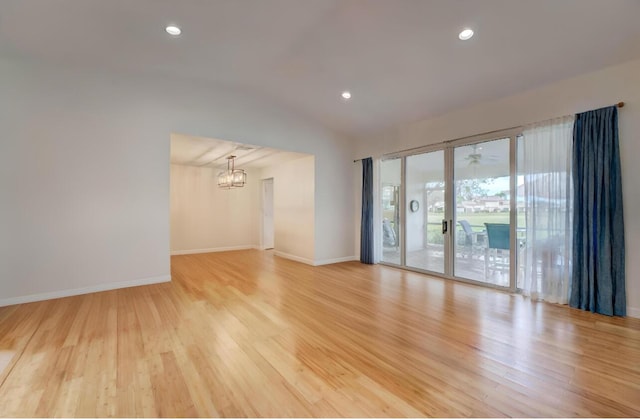 empty room with vaulted ceiling, an inviting chandelier, and light hardwood / wood-style flooring