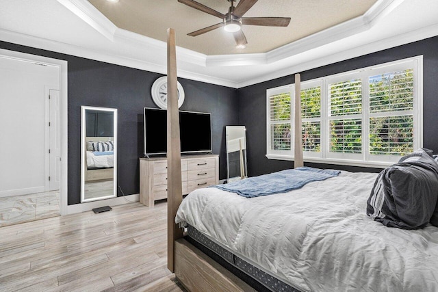 bedroom featuring a ceiling fan, a tray ceiling, wood finished floors, and crown molding