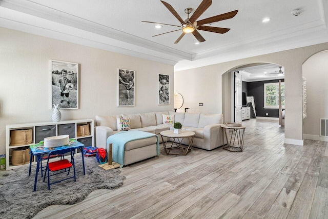 living room featuring ceiling fan, a raised ceiling, light wood-type flooring, and ornamental molding