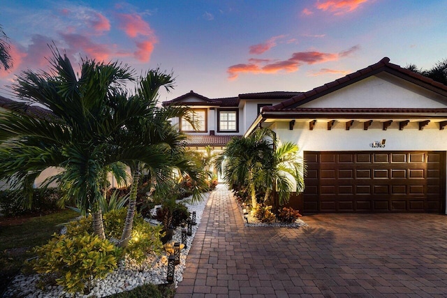 mediterranean / spanish-style home featuring a tile roof, decorative driveway, a garage, and stucco siding