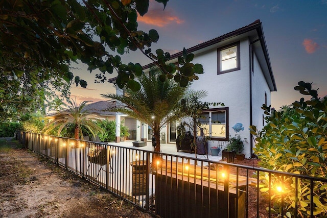 back of property at dusk with a patio area, stucco siding, and fence