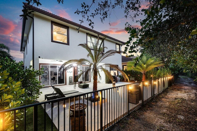 back of house at dusk featuring stucco siding, a patio, and fence