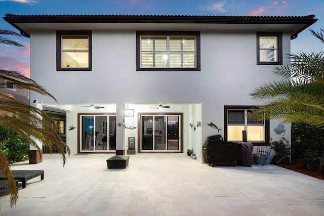 back of house at dusk with stucco siding and a patio