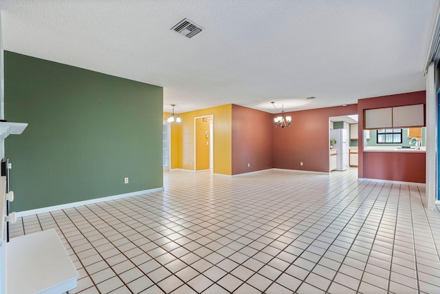 unfurnished living room featuring sink, light tile patterned floors, a textured ceiling, and a chandelier