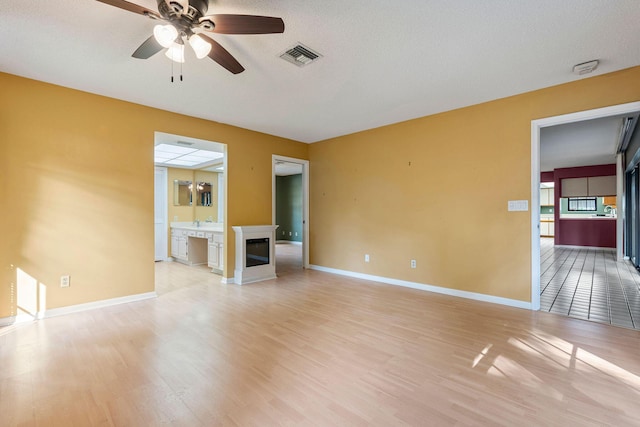 unfurnished living room with a textured ceiling, light hardwood / wood-style flooring, and ceiling fan