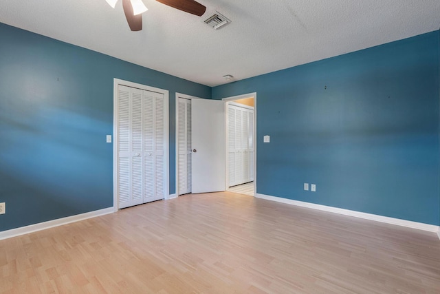 unfurnished bedroom featuring ceiling fan, a textured ceiling, light hardwood / wood-style flooring, and two closets