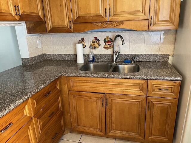 kitchen with light tile patterned floors, sink, dark stone counters, and tasteful backsplash