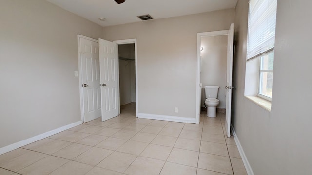 unfurnished bedroom with ensuite bathroom, ceiling fan, a spacious closet, light tile patterned flooring, and a closet