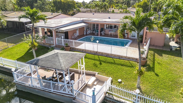 rear view of property featuring a gazebo, a fenced in pool, and a lawn