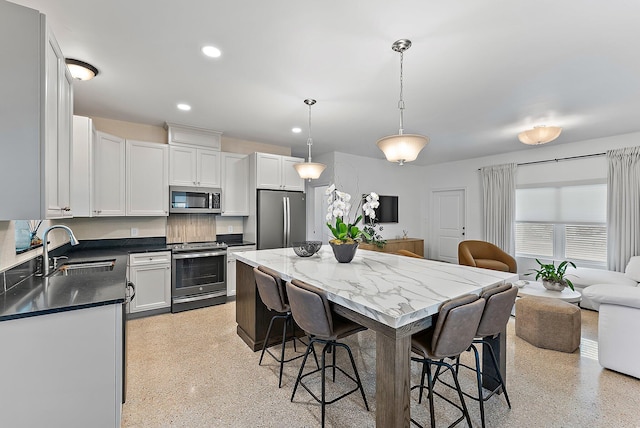 kitchen with a kitchen bar, appliances with stainless steel finishes, sink, pendant lighting, and white cabinetry