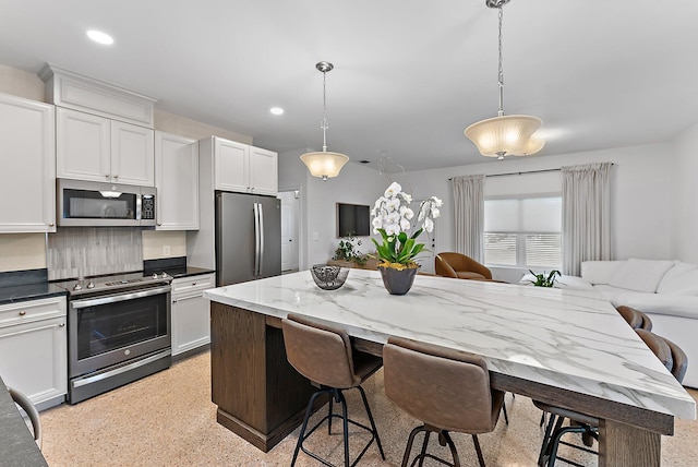 513 E Whitney Dr, Jupiter, FL 33458 - kitchen with stainless steel appliances, a kitchen breakfast bar, dark speckled floor, white cabinetry, and decorative light fixtures