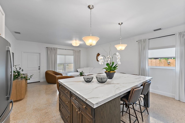 kitchen featuring a kitchen bar, stainless steel fridge, light stone countertops, dark brown cabinetry, and pendant lighting