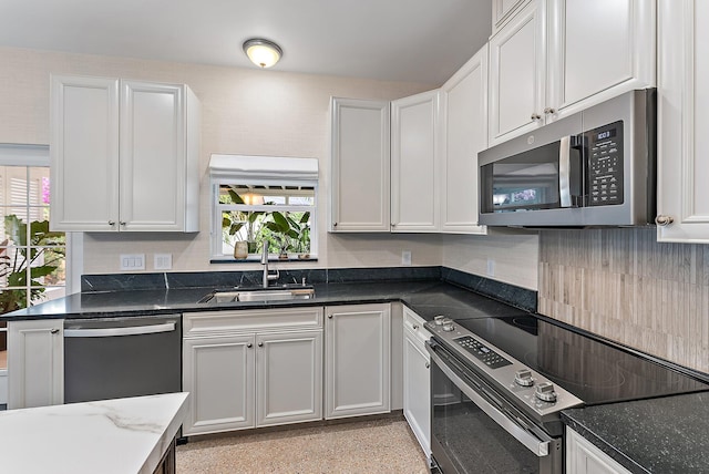 kitchen with stainless steel appliances, white cabinetry, a wealth of natural light, and dark stone countertops