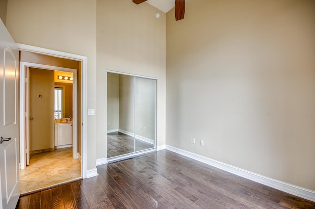unfurnished bedroom with high vaulted ceiling, wood finished floors, a closet, baseboards, and ceiling fan