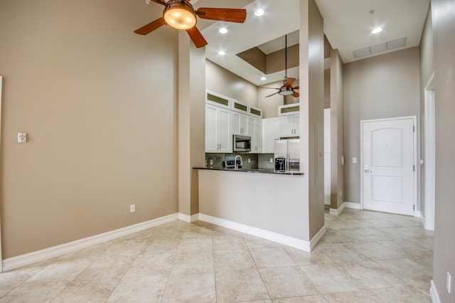kitchen featuring a ceiling fan, appliances with stainless steel finishes, dark countertops, a high ceiling, and white cabinetry