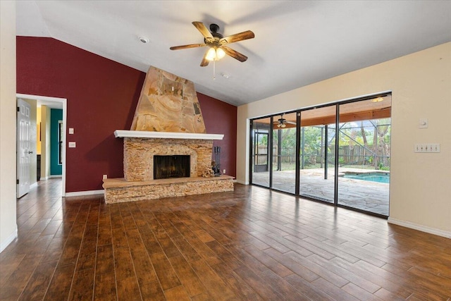 unfurnished living room with lofted ceiling, a stone fireplace, dark wood-type flooring, and ceiling fan