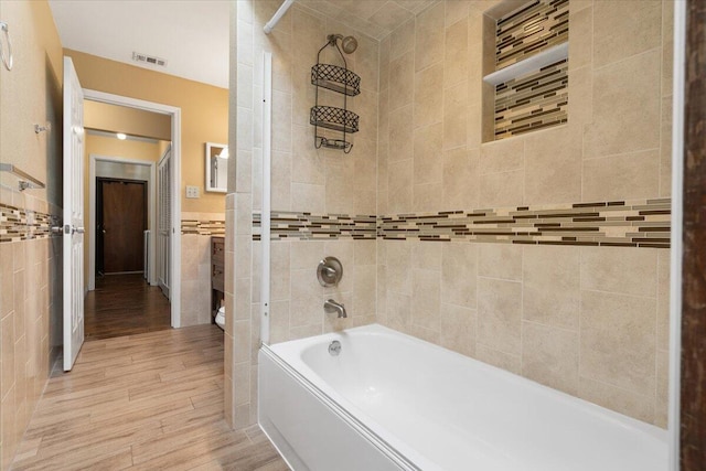 bathroom with tiled shower / bath, hardwood / wood-style floors, and tile walls