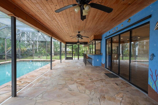 view of swimming pool with a bar, a patio area, ceiling fan, and glass enclosure