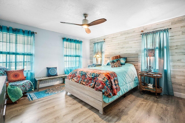 bedroom with hardwood / wood-style floors, multiple windows, wooden walls, and ceiling fan