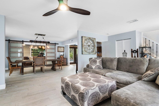 living room with ceiling fan, a barn door, and light wood-type flooring