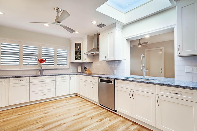 kitchen featuring light wood-type flooring, stainless steel dishwasher, wall chimney exhaust hood, sink, and white cabinets