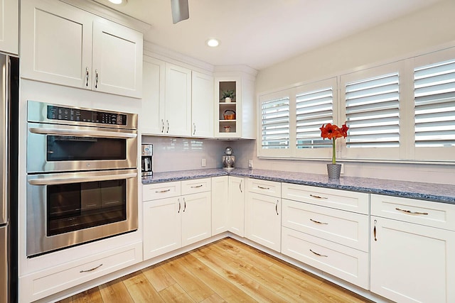 kitchen featuring white cabinetry, tasteful backsplash, light hardwood / wood-style flooring, double oven, and dark stone counters