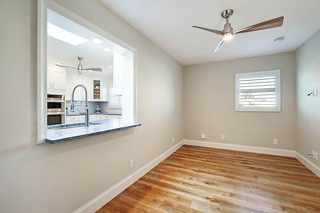 unfurnished dining area with ceiling fan, light hardwood / wood-style floors, sink, and a skylight