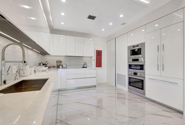 kitchen with decorative backsplash, light stone counters, white cabinetry, and sink