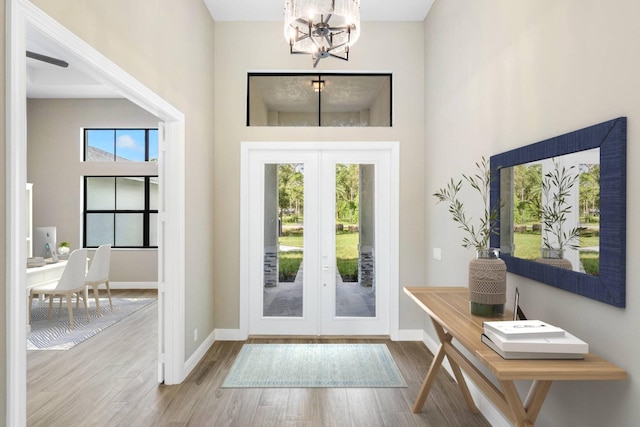 entryway featuring french doors, a healthy amount of sunlight, wood finished floors, and an inviting chandelier