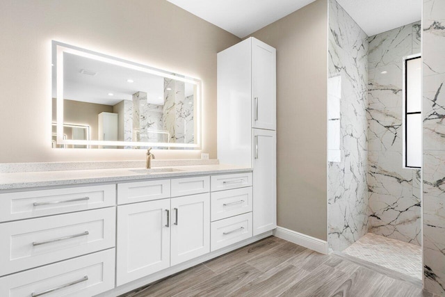 full bath with baseboards, vanity, a marble finish shower, and wood finished floors