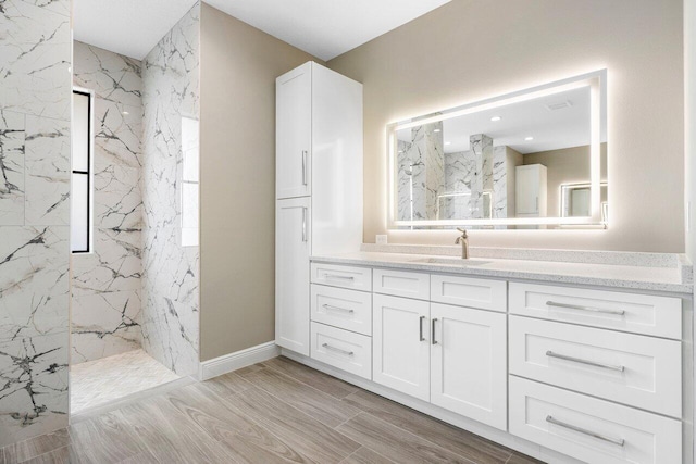 full bath with a marble finish shower, baseboards, and vanity