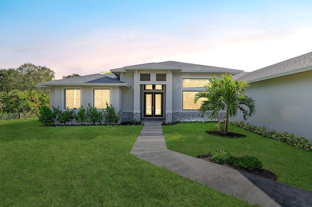 prairie-style home with french doors, a front lawn, stone siding, and stucco siding