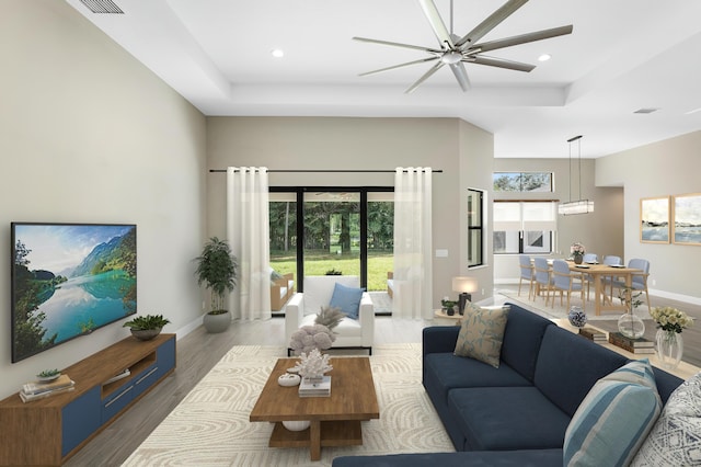 living area featuring a wealth of natural light, a tray ceiling, baseboards, and wood finished floors