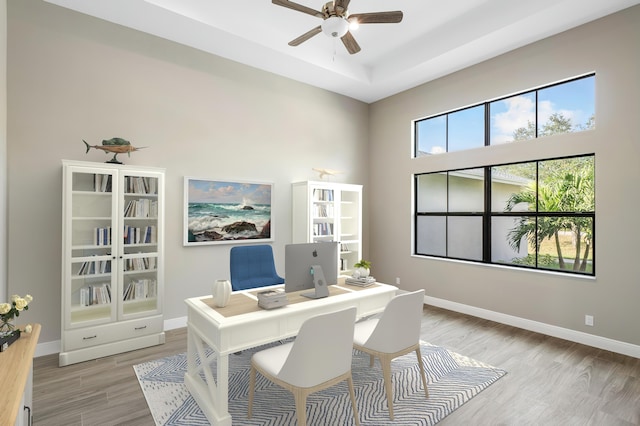 home office with a ceiling fan, light wood finished floors, and baseboards