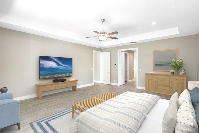 bedroom with light wood-type flooring, a raised ceiling, visible vents, and baseboards