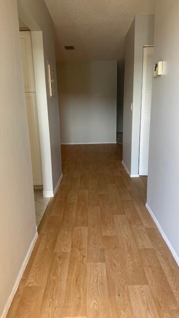 hallway with a textured ceiling and light hardwood / wood-style flooring