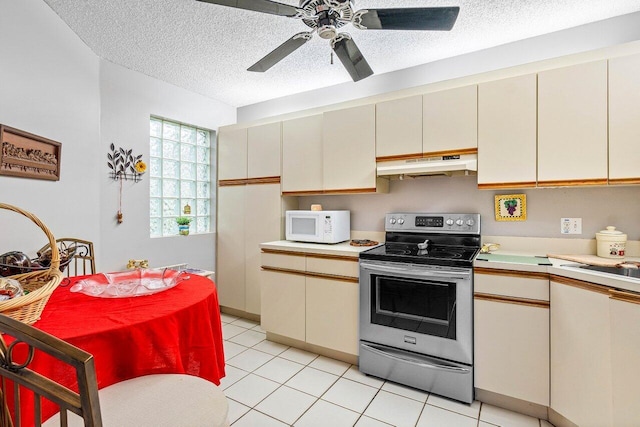 kitchen featuring electric range, light tile patterned floors, a textured ceiling, and cream cabinetry