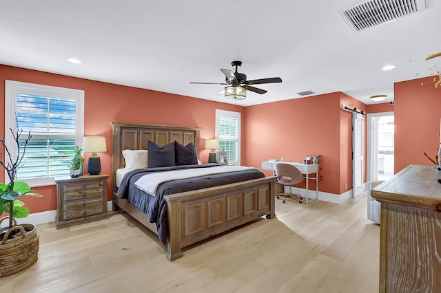 bedroom with light wood-type flooring, ceiling fan, and a barn door