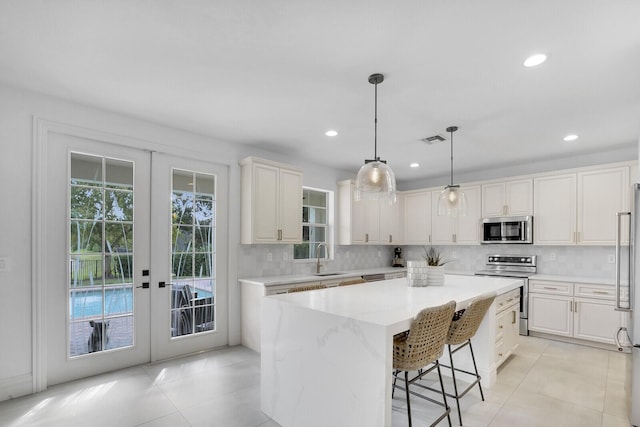 kitchen featuring french doors, sink, stainless steel appliances, pendant lighting, and a kitchen island